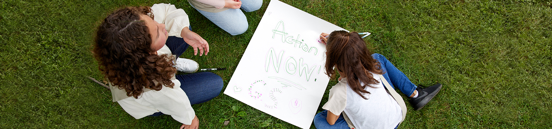  Three girls creating a poster that says, "Action now! GS" 