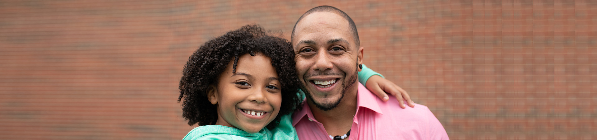  a girl with her arm around her dad's shoulder; they're both smiling at the camera 