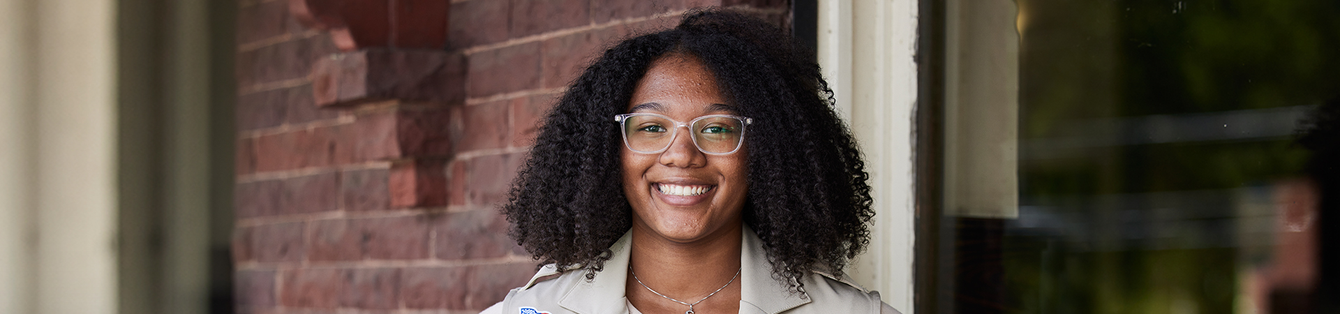  A Girl Scout beaming at the camera in front of an older brick building 
