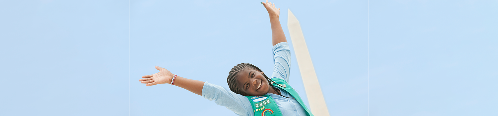  A smiling girl posing with her arms in the air in front of the Washington Monument 